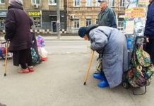 «Всю пенсию отдаю, вдвоём выживаем»: как живут люди, каждый день ждущие на остановке в Ростове бесплатного обеда Сгорбленная старушка стоит, облокотившись о столб. Сумка рядом. Парни кладут туда еду. //Фото Инна Лебедева