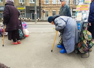 «Всю пенсию отдаю, вдвоём выживаем»: как живут люди, каждый день ждущие на остановке в Ростове бесплатного обеда Сгорбленная старушка стоит, облокотившись о столб. Сумка рядом. Парни кладут туда еду. //Фото Инна Лебедева